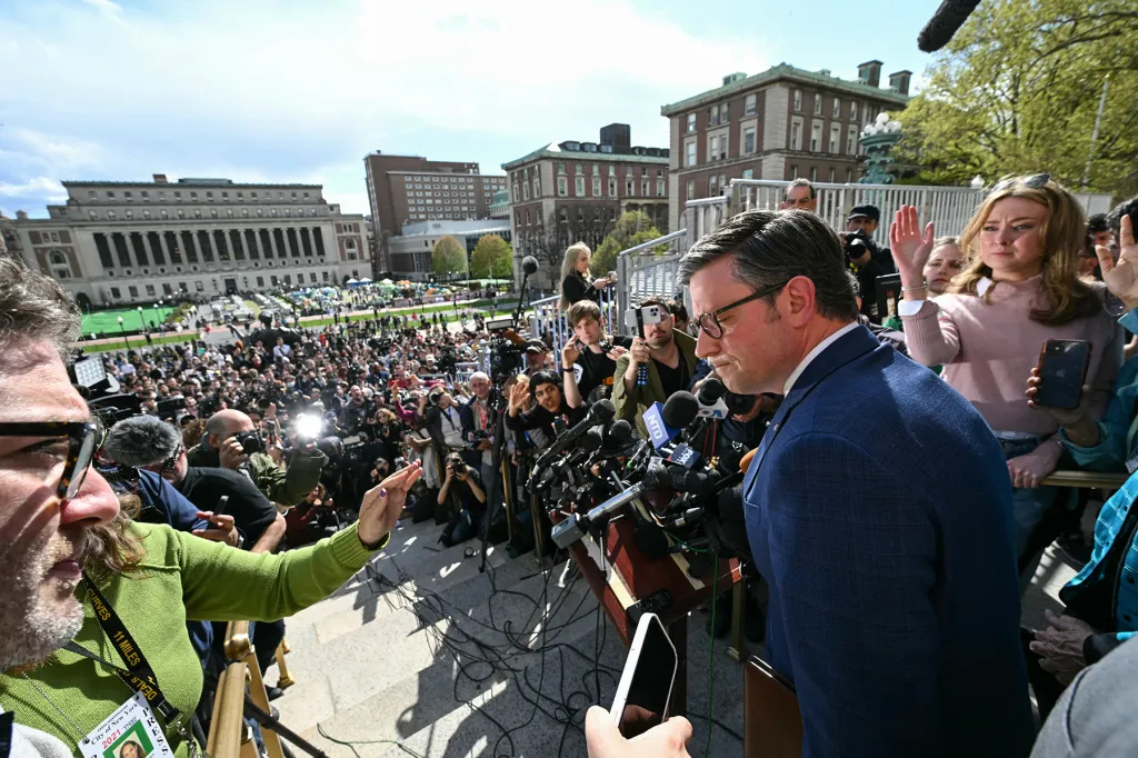 Reporters gather outside Columbia's encampment, visible in the background. 